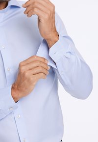 Lichtblauw overhemd met knoopmanchetten, gladde stof, lange mouwen en een casual kraag, met een getailleerd ontwerp en een effen textuur.
