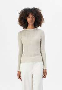 Lys beige langermet topp med fin ribbestruktur, rund hals, og tettsittende silhuett. Brukt med hvite vide bukser.