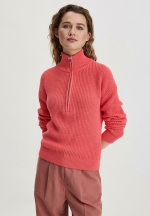 Pull en tricot corail avec col haut et fermeture à demi-glissière. Comprend des poignets et un ourlet côtelés, avec un design de tissu texturé.