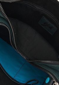 Interno di una borsa in tessuto nero con una fodera color teal. Presenta tasche con zip e un'etichetta in pelle nera texturizzata. Tessuto complessivo liscio e morbido.