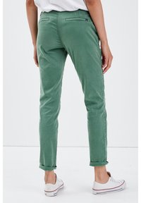 Groene chino's met een slim fit, opgerolde pijpen en achterzakken. Gemaakt van zachte katoen, ontworpen voor casual gebruik. Witte sneakers zichtbaar.