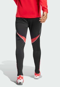 Black athletic pants with red accents, featuring a slim fit, subtle texture, and side zippers. Paired with red athletic footwear.