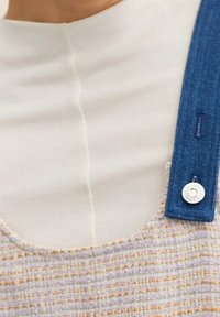 Collier ras du cou à sangle en denim avec un haut en tissu crème clair, présentant un vêtement texturé aux motifs violets et oranges, mettant en valeur un bouton métal circulaire.