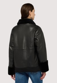 Czarna skórzana kurtka z miękkim czarnym futrzanym kołnierzem, ryflowanym dołem i mankietami. Charakteryzuje się gładką fakturą i lekko oversize'owym krojem.