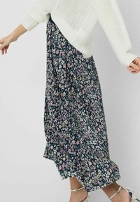 Gonna maxi floreale in blu scuro, con piccoli fiori colorati. Tessuto leggero e plissettato con una vestibilità comoda, abbinata a un top bianco accogliente.