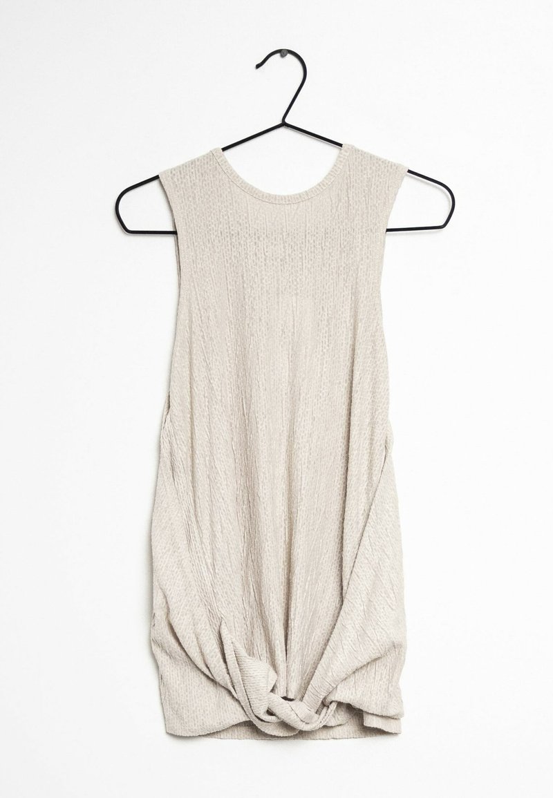 Haut sans manches beige clair en tissu texturé, avec un col rond et un détail noué en bas. Suspendu à un crochet noir.