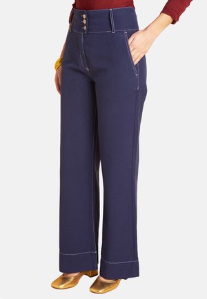 Woman wearing navy wide-leg pants with high waistband and three buttons, paired with gold low heel shoes and a red top.