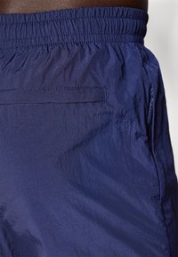 Tamnoplave kratke hlače od lagane tkanine, s elastičnom gumicom u struku, stražnjim džepom i bočnim detaljem sa zatvaračem. Glatka tekstura.