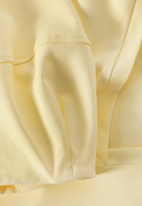 Weicher gelber Stoff mit sichtbaren Nähten und Nahtdetails, zeigt sanfte Falten und eine glatte Textur.