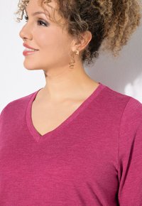 V-hals, kortdynamisch top in een levendige fuchsia kleur. Zacht, gestructureerd materiaal met een relaxte pasvorm. Accessoires bestaan uit kleine gouden oorringen.