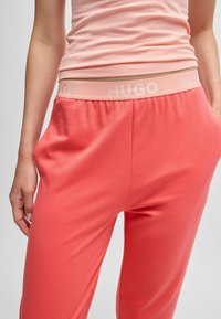Koraalkleurige sweatpants met een elastische tailleband met het "HUGO"-logo. De stof lijkt zacht met een gladde textuur en een ontspannen fit.