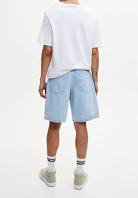 Světle modré denimové šortky volného střihu, zadní kapsy a bílé tričko s kulatým výstřihem. Na sobě má béžové tenisky a bílé ponožky s černými pruhy.