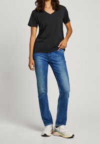 Svart v-ringad t-shirt, blå raka jeans och mångfärgade träningsskor. Outfiten har en avslappnad och luftig passform.