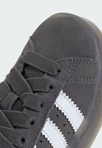 Lähikuva mustastat samettikengistä, joissa on teksturoidut mustat nauhat ja kaksi valkoista siksak-reunalla varustettua raitaa sivulla.