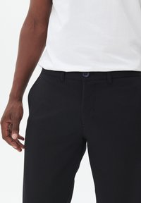 Zwarte broek van lichtgewicht stof, met een gladde voorkant, standaardzakken en een knoopsluiting bij de taille.