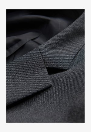 Op maat gemaakte zwarte stof met een subtiele weefpatroon, voorzien van een scherpe kraag en een gladde voering. Close-up van het gestructureerde reversdetail.