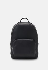 Zaino in pelle nera con superficie testurizzata, forma rotonda, tasca frontale con zip e manico superiore. Logo discreto nella parte anteriore inferiore.