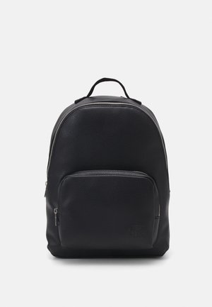 Zaino in pelle nera con superficie testurizzata, forma rotonda, tasca frontale con zip e manico superiore. Logo discreto nella parte anteriore inferiore.