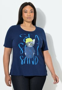 Merensininen t-paita pehmeää, kevyttä kangasta, jossa on kuva keltaiseen hattuun pukeutuneesta kissasta ja teksti "SEA SAND". Pyöreä pääntie, lyhyet hihat.