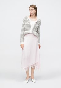 Γκρι και λευκή ριγέ ζακέτα με υφή πλεκτού, σε συνδυασμό με ροζ σατέν φούστα με δαντελένιο τελείωμα και λευκά παπούτσια με μυτερό δάχτυλο.