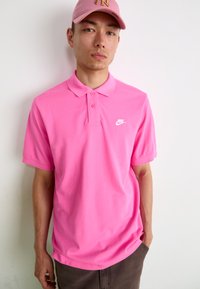 Nike polo shirt i strålende pink bomuld med krave, korte ærmer, tre-knaps placket og hvidt logo på venstre bryst.