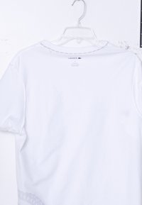 White Lacoste t-shirt hanging on a white plastic hanger with visible brand label and logo on the back collar area.