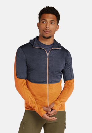Gewatteerde jas met een blauwe bovenkant en een oranje onderkant. Gemaakt van een gestructureerde stof met een rits aan de voorkant en duimgaten in de mouwen.