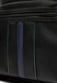 Schwarze Ledertasche mit strukturierter Oberfläche, blauen und grünen gestreiften Akzenten an den Seiten und einem Reißverschluss oben.