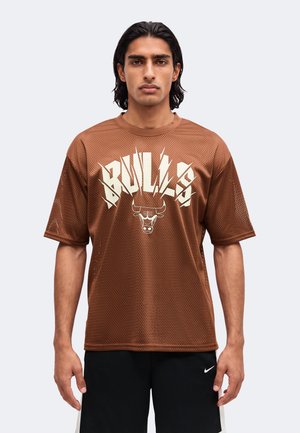 Άνδρας φοράει καφέ διαπνέον μπλουζάκι με "BULLS" και λογότυπο ταύρου στο μπροστινό μέρος, στέκεται με τα χέρια χαλαρά δίπλα στο σώμα.