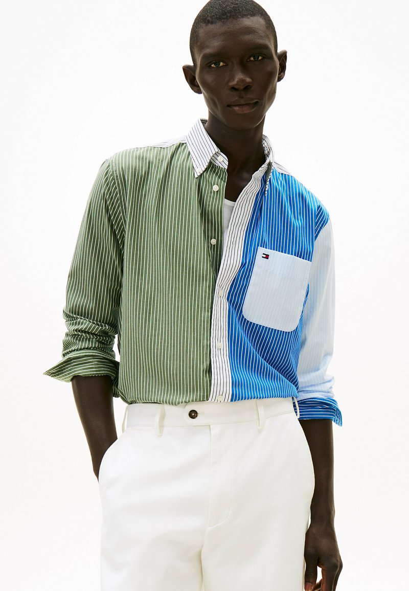Kolorowa koszula na guziki z pionowymi paskami w zielonym, niebieskim i białym kolorze. Posiada kieszeń na piersi oraz kontrastujący kołnierz.