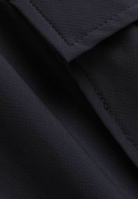 Tissu bleu marine avec une texture de maillage subtile, présentant des sections superposées et une couture propre et droite le long des bords.