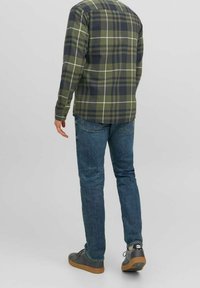 Grünes und marineblaues kariertes Flanellhemd mit langen Ärmeln, kombiniert mit schmal geschnittenen blauen Jeans und grauen Sneakers mit braunen Sohlen.