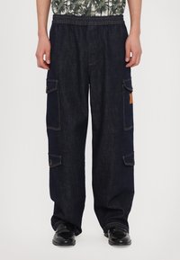 Pantaloni cargo bleu închis din material denim, cu un tiv elastic, mai multe buzunare laterale și detalii de cusătură contrastante.
