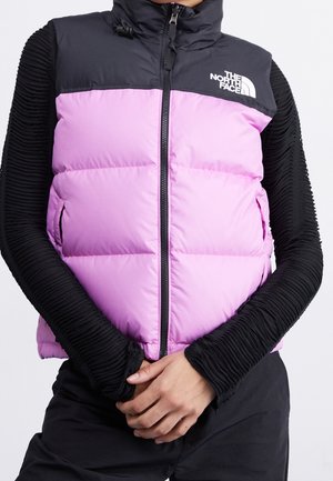 Personne portant un haut noir à manches longues et un gilet matelassé noir et rose zippé avec le logo The North Face sur la poitrine.
