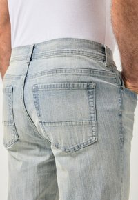 Jeans de mezclilla azul claro con corte recto, cintura de tiro medio, bolsillos traseros y sutil textura vertical. Detalles mínimos de costura.