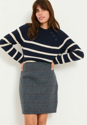 Marineblauer Strickpullover mit weißen Streifen und Knopfdetails, kombiniert mit einem grauen karierten Bleistiftrock mit roten und blauen Linien.