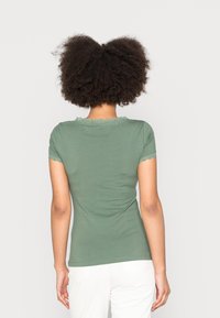 T-shirt verde in cotone a maniche corte con pizzo sul collo e sui bordi delle maniche, design aderente e texture liscia. Vista posteriore mostrata.