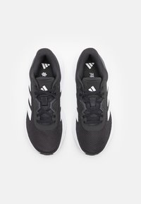 Black athletic shoes with a mesh upper, white accents, lace-up design, and a textured sole. Features a padded collar and logo on the tongue.