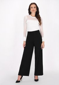 Maglia bianca con maniche lunghe e trasparenti a pois, abbinata a pantaloni neri a gamba larga a vita alta e tacchi neri.