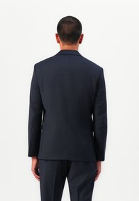 Blazer ajusté bleu marine avec une finition lisse, une forme structurée et un motif à carreaux subtil ; il présente des revers crantés et des poignets boutonnés.