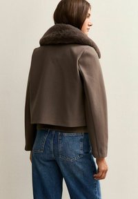 Bruine cropped jas met een faux fur kraag, voorzien van lange mouwen en een soepele textuur, gecombineerd met hoge taille blauwe denim jeans.