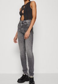 Mustaton hihaton body, jossa on aukko yksityiskohtana, yhdistettynä harmaisiin slim-fit farkkuihin ja mustiin korokepolkimiin. Suora kangas, jossa on hillitty tekstuuri.