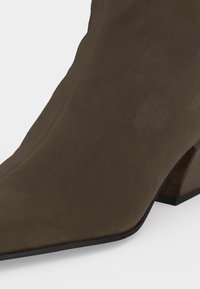Bottine en daim marron avec bout pointu et talon bloc sur fond blanc.