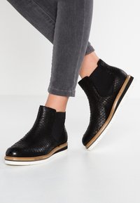 Botas negras hasta el tobillo con un patrón de piel de reptil texturizado, paneles laterales elásticos y suelas de goma blanca con un ligero borde marrón.