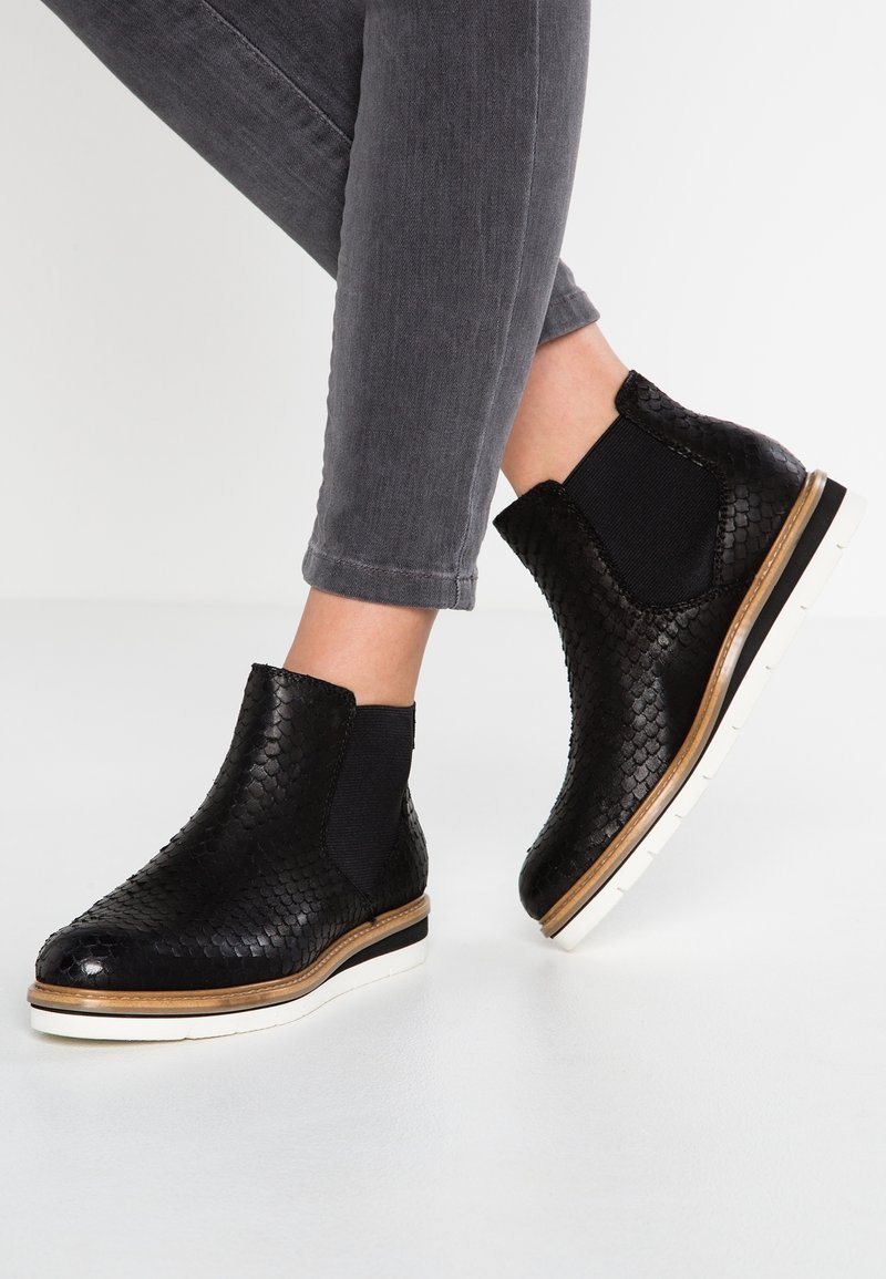 Botas negras hasta el tobillo con un patrón de piel de reptil texturizado, paneles laterales elásticos y suelas de goma blanca con un ligero borde marrón.
