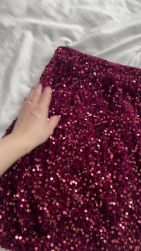 Burgunderstoff dekket med roségullpaljetter, med en myk tekstur og en skinnende overflate, med en hånd delvis synlig over.