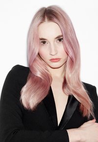 Model met lang, golvend haar dat overgaat van roze naar blond. Draagt een zwart, diep V-hals topje met satijnen accenten tegen een witte achtergrond.