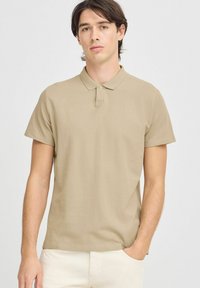 Polo shirt in cotone beige con colletto e maniche corte. Presenta un logo sottile sul petto e una vestibilità comoda.