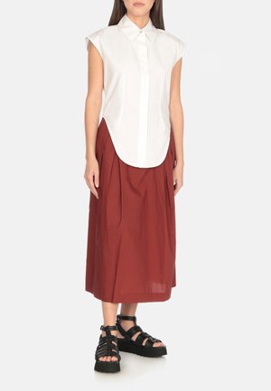 Camicia bianca a maniche corte, abbinata a una gonna pieghettata rossa ruggine di lunghezza al ginocchio e sandali neri con cinturini e suola spessa.