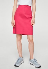 Jupe rose longueur genou en tissu structuré, dotée d'une taille ajustée et d'une silhouette slim. Associée à des chaussures de sport bleu clair.